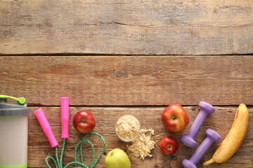 Bowl with protein powder, apples, banana, skipping rope, dumbbells and bottle on wooden background