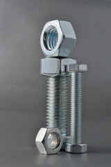 composition of new bolts and nuts of different sizes on a gray background.