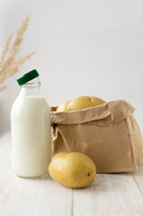 Potato milk in a glass bottle on a white wooden background. New, young potatoes in a kraft paper...