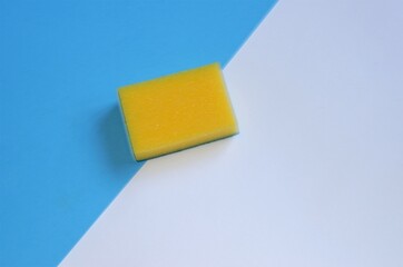 one yellow-colored sponge for cleaning and washing on a white-blue background, creative photo Tool for cleaning, cleanliness and cleaning.