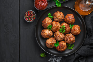 Fried meatballs with basil in a black plate on a dark background.