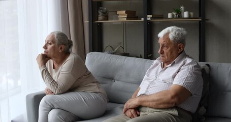 Sad resentful old age family couple sit on couch at living room separately feel offence misunderstanding avoid talking ignoring each other. Upset mature husband wife having problem in relationship