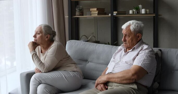 Sad resentful old age family couple sit on couch at living room separately feel offence misunderstanding avoid talking ignoring each other. Upset mature husband wife having problem in relationship