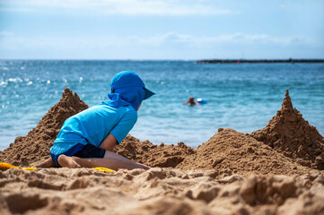 Kind in Sonnenschutzkleidung baut eine Sandburg an einem schönen Strand