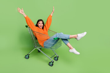 Portrait of attractive cheerful childish foolish girl riding cart having fun good mood isolated over bright green color background