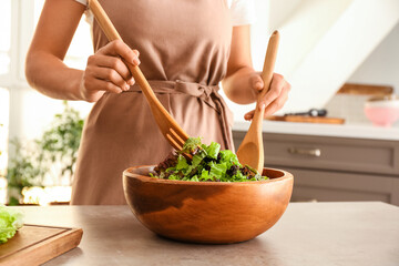 Woman preparing tasty salad with fresh lettuce leaves in kitchen