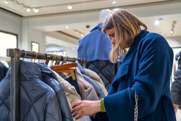 Obraz premium Portrait of happy woman customer chooses jacket in clothing store. Customer making choices in shop with clothes