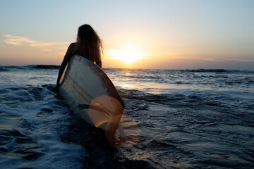 beautiful girl with a surfboard at sunset.
