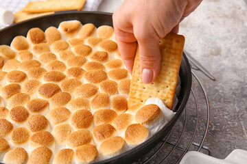 Woman eating delicious S'mores dip at table, closeup - obrazy, fototapety, plakaty