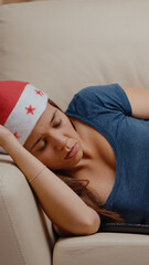 Close up of woman falling asleep while watching television on couch. Festive person wearing santa hat and feeling sleepy on christmas eve. Adult sleeping on sofa with bowl of chips