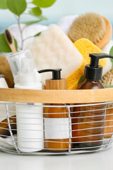Basket with bottles of cosmetic products and bath sponges on table, closeup