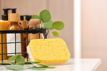 Bath sponge, eucalyptus branch and basket with bottles of cosmetic products on table
