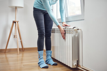 Woman heating her hands on the radiator during cold winter days. - obrazy, fototapety, plakaty
