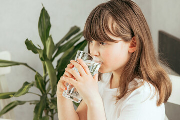 A girl in the kitchen drinks clean water from a glass glass. The importance of water for children,...