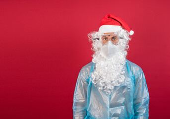 Fototapeta na wymiar Man, in front of a red background, disguised as Santa Claus, wearing glasses, mask, and protective coat for Covid 19.
