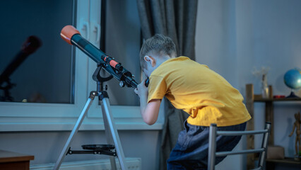 Cute boy is looking through a telescope at the night starry sky. Children's scientific hobbies and...