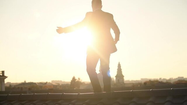 Successful man in black formal wear dancing on the roof in the city at sunny daytime. Enjoying freedom. Conception of achievement and inspiration