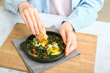 Woman eating tasty Shakshouka at kitchen table, closeup
