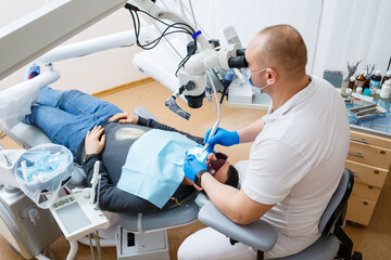 Fototapeta premium The dentist treats his patient's teeth with a microscope. The dentist treats the patient's mouth. Dental care