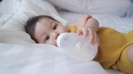 asian baby toddler infant playing on bed walking around then drinking mother food milk from bottle. baby skill development holding milk bottle.