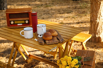 Tasty buns with hot chocolate and radio receiver on table in autumn forest