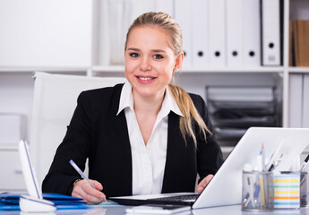 Young smiling businesswoman sitting at working place in office