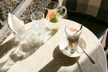 Glass of tasty coffee and jug with water on table in outdoor cafe