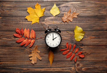 Alarm clock and autumn leaves on wooden background. Daylight saving time end