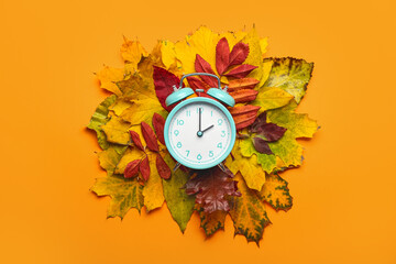 Alarm clock and autumn leaves on color background. Daylight saving time end