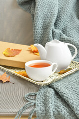Tray with tea pot, cup of hot beverage and autumn leaves on sofa in room