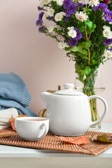 Tea pot, cup of hot beverage, Chrysanthemum flowers and autumn leaves on table near beige wall