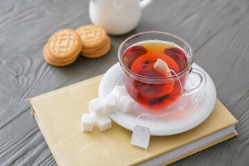 Glass cup of hot tea and book on grey wooden background
