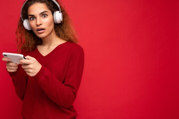 Photo of beautiful young brunette curly shocked amazed woman wearing dark red sweater isolated over...