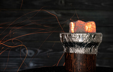 hot burning red coals for a hookah with sparks and smoke on a dark background.Traditional Asian relaxation. Space for text