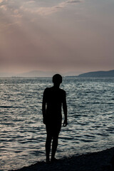 Contemporary art dramatic portrait silhouette a man at the sea in rays of the setting sun against the backdrop dark waves and beautiful evening sky