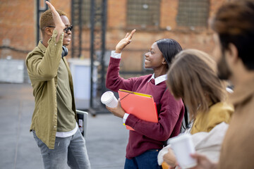 Black girl and guy holding hands of each other near their multiracial friends. Concept of education and learning. Idea of student lifestyle. Young smiling students at university campus