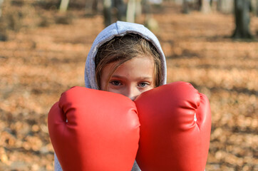 Little adorable girl child in a tracksuit, with a hood on his head, in red boxing gloves, boxing on...