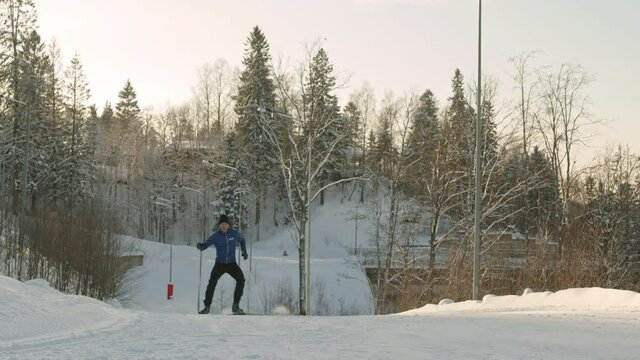 Low angle locked-down of young Caucasian man wearing sporty outfit, skiing on white snow by forest outdoors, then falling and getting up