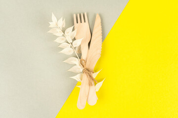 Wooden cutlery, fork and takeaway knife with a dry branch of a flower on lgray and yellow background. Organic and ecological zero waste.