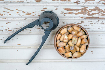 hazelnuts with nutshells in a bowl and nutcracker on a wooden table