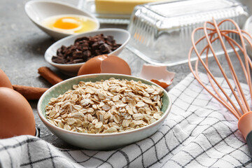 Bowl with oatmeal flakes for preparing homemade cookies on grey background