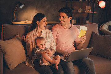 Portrait of full amazed family motherhood fatherhood parenthood boyfriend girlfriend cuddling baby buying flight tickets at home indoors