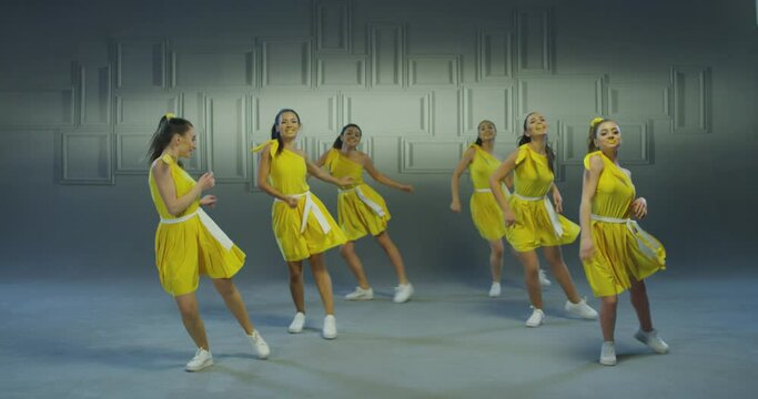 4k Group of beautiful , funny, stylish girls in yellow dresses dancing inside pavilion with grey background  . Synchronized dance of female ensemble for video clip  Woman dancers with the same outfit 