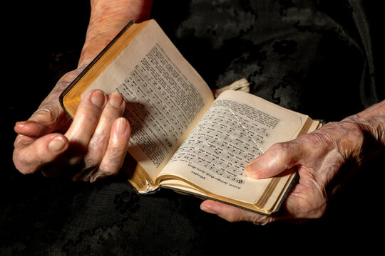 Frauenhände, Seniorin, hält Buch vor dunklem Hintergrund.