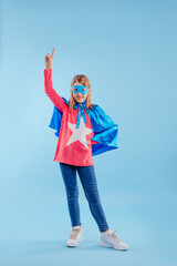 Little girl wearing super hero costume pointing up on blue background