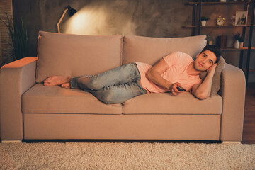 Portrait of attractive peaceful calm guy lying on divan watching tv show late night lamp lighting...