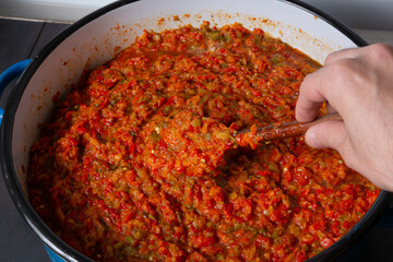 Hand mixing Ajvar traditional Balkan food in a big pot on the stove. Process of making delicious refection from mashed and cooked peppers at home