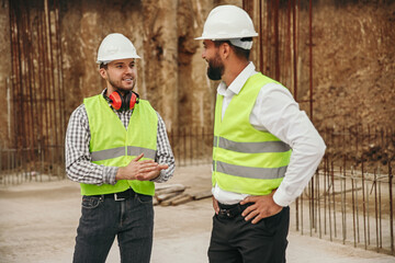 young male engineers discussing construction details near unfinished building