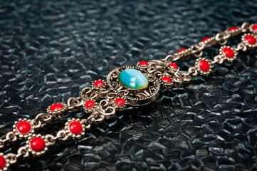 Metal women's wrist bracelet with an emerald and red stones on a dark background.