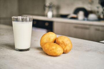 A transparent glass with potato milk on the table next to the potato tubers. 